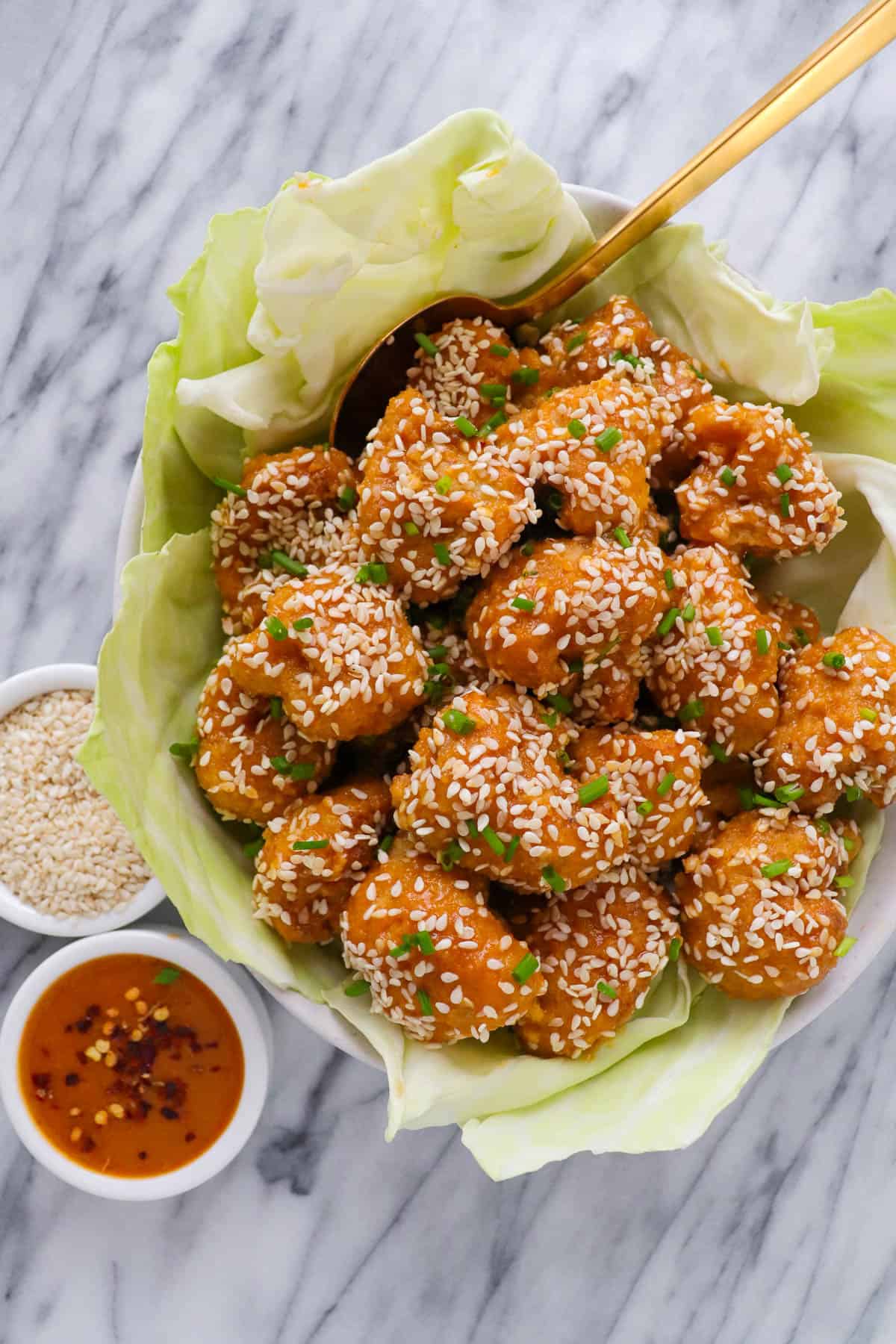 Orange sesame cauliflower in a bowl with sesame seeds + extra sauce on the side.