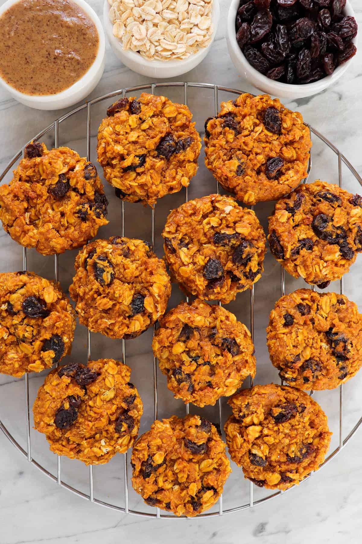 Sweet potato cookies on cooling rack with nut butter, oats and raisins in mini bowls on the side.