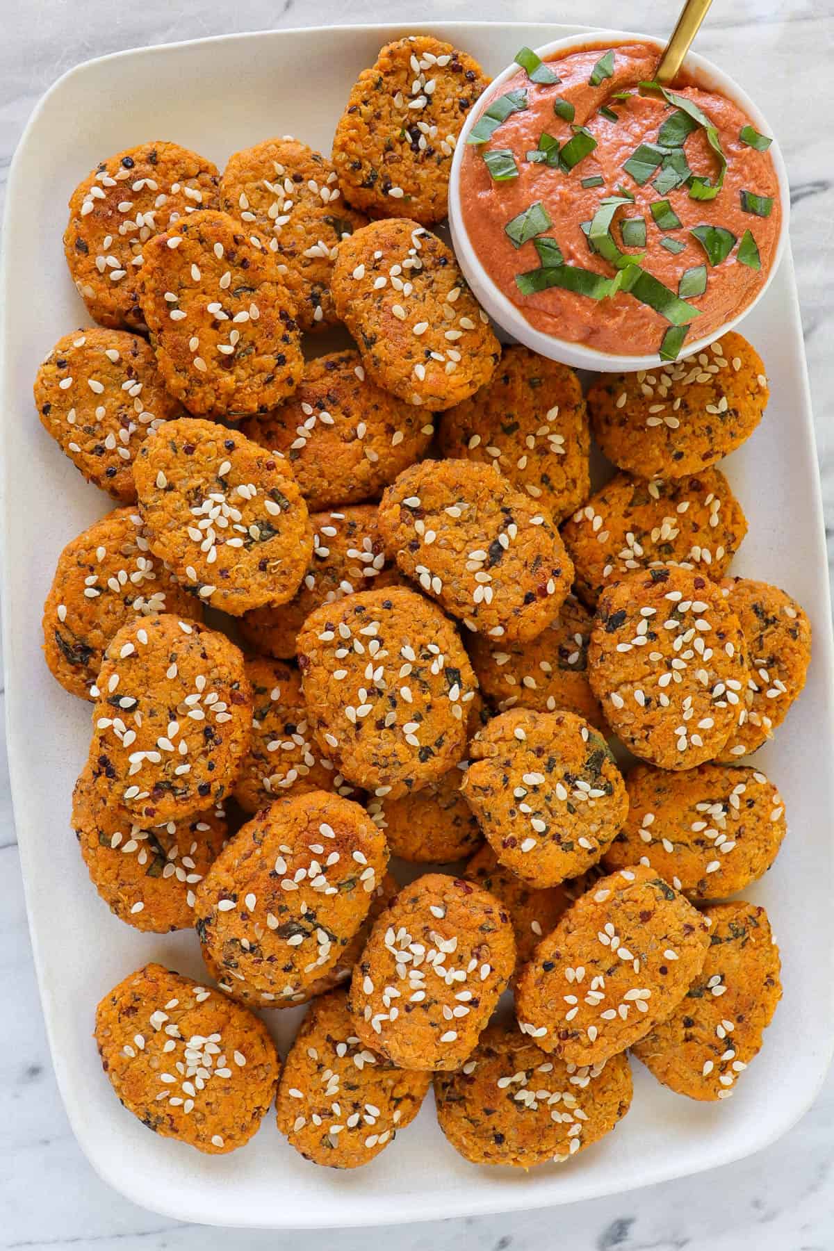 Sweet potato bites on long plate with creamy tomato dip with a gold spoon.