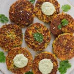 Cooked fritters on a plate with coriander leaves, avocado dip dolloped on top and sprinkled with sesame seeds.