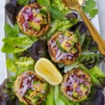 Tuna cakes on lettuce leaves with chopped avocado, red onion and chili flakes on top of each one. Lemon wedge and gold cutlery on the side.