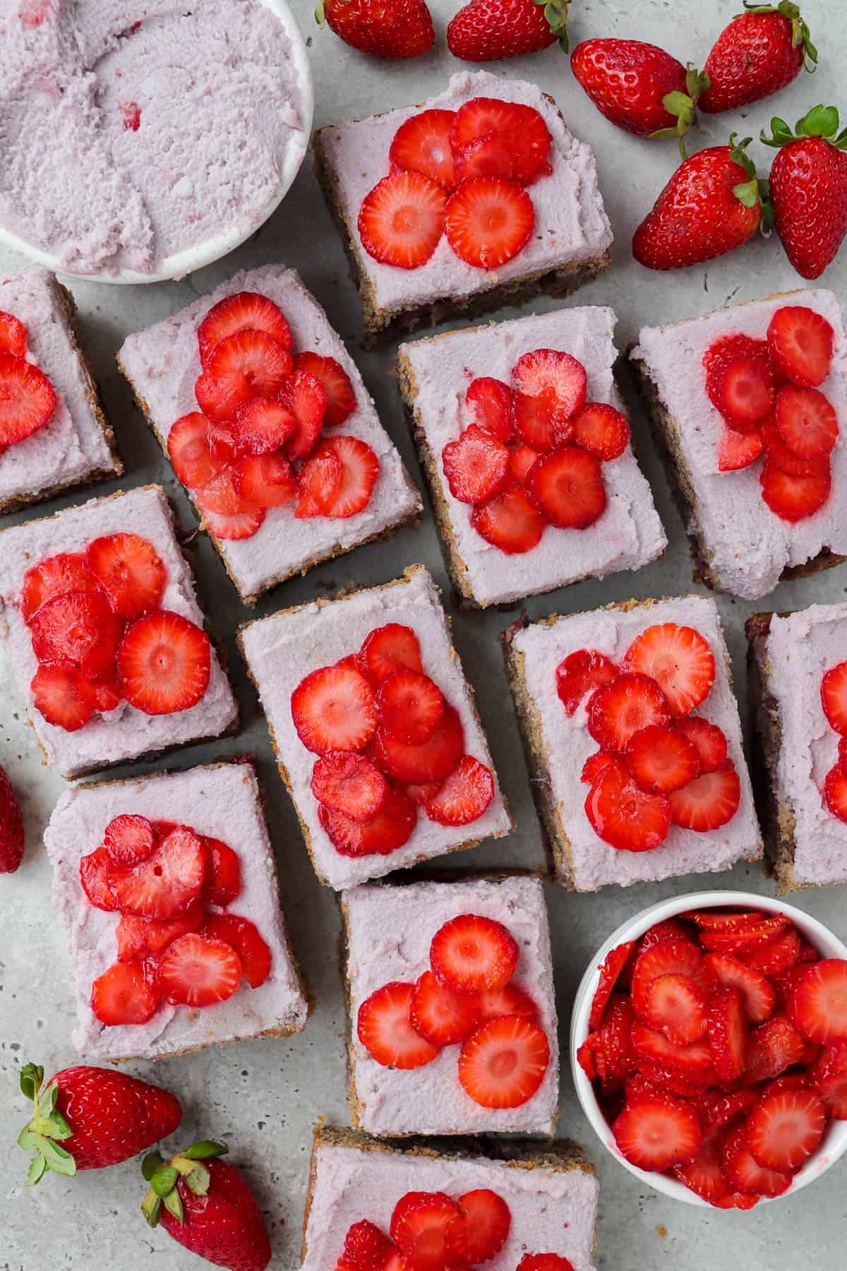 Frosted cake topped with sliced strawberries and cut up into small rectangle slices.