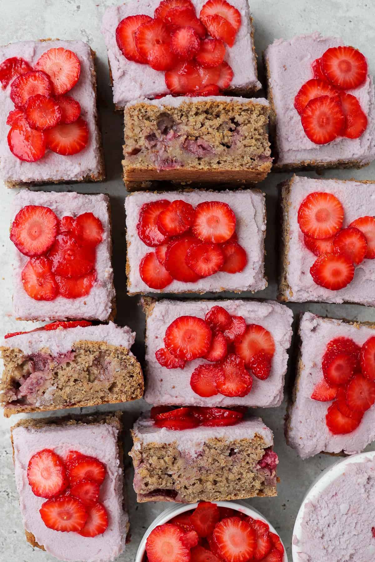 Frosted cake topped with sliced strawberries and cut up into small rectangle slices. Three slices turned on the side or an inside view.