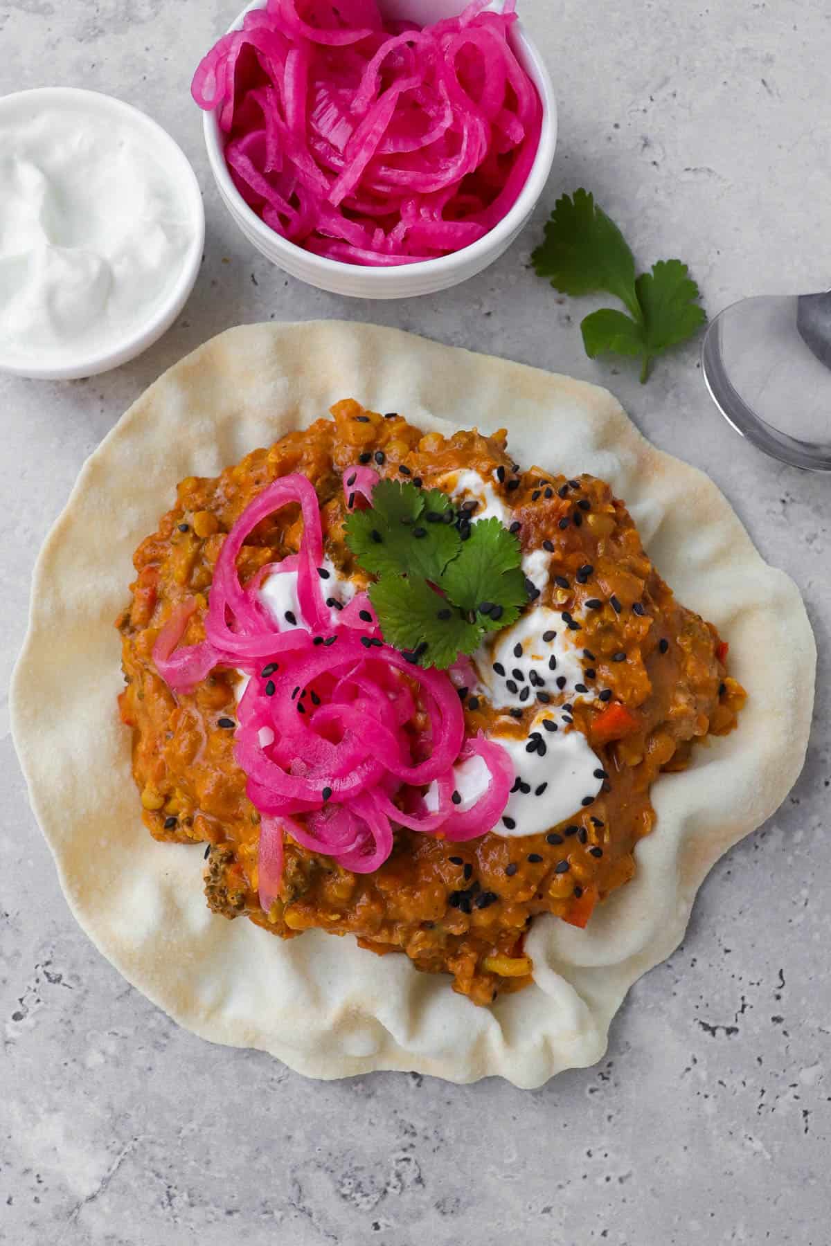 Dahl served in a papadum with pickled onions, yoghurt, coriander leaves and black sesame seeds for garnish.