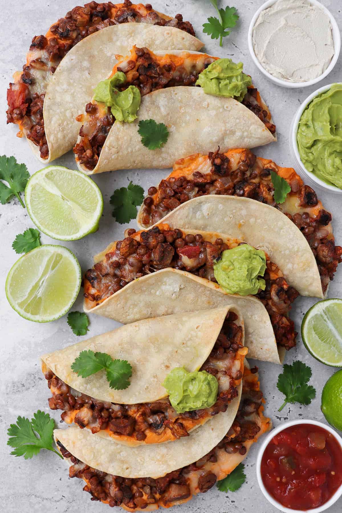 Baked tacos topped with guacamole. Fresh limes and salsa on side for decoration.