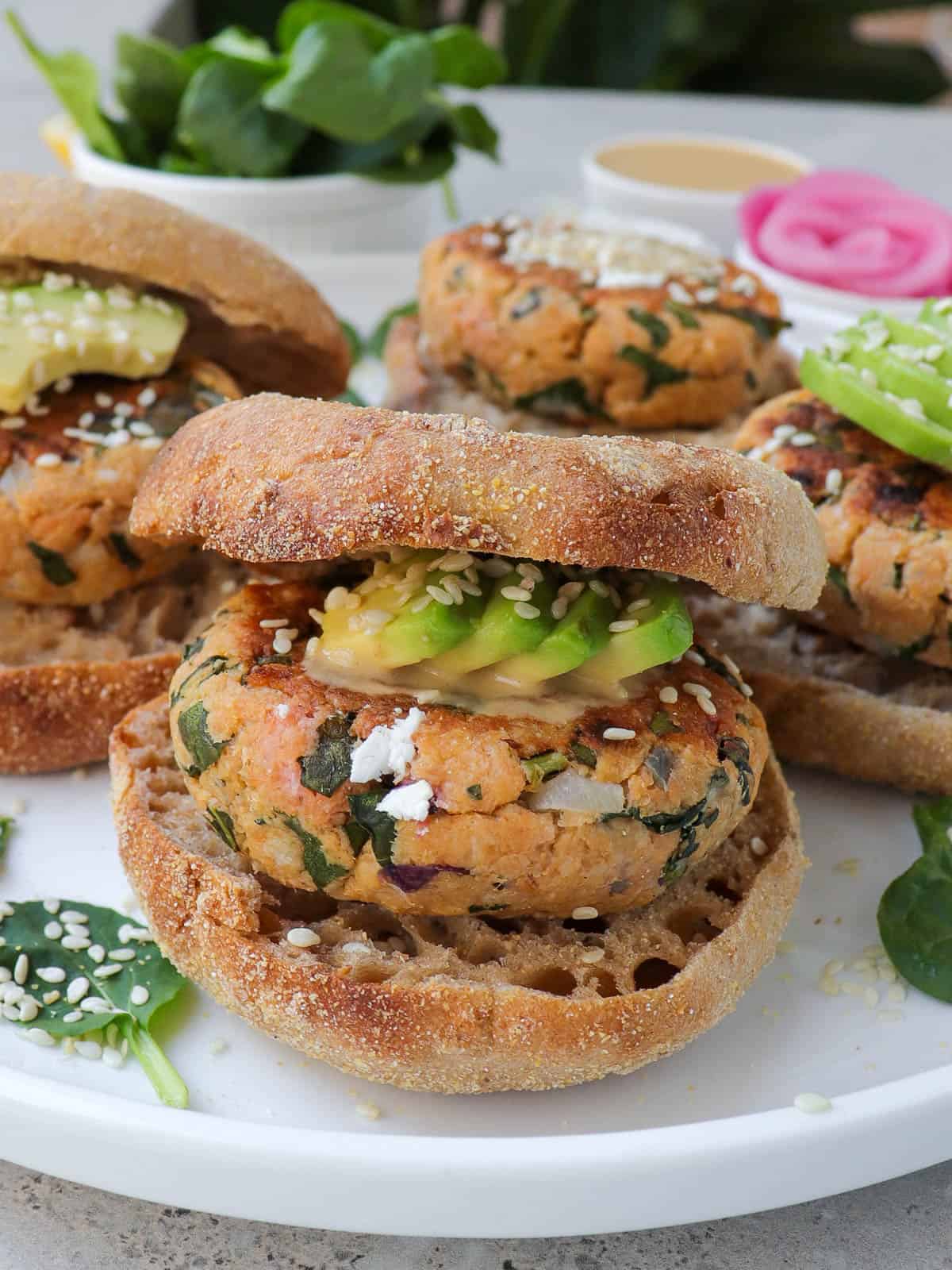 Side view of salmon burger in English muffin topped with avocado and sesame seeds.