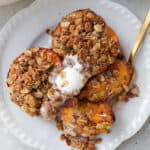 Air fryer peaches on plate with ice cream and fork cutting into one.