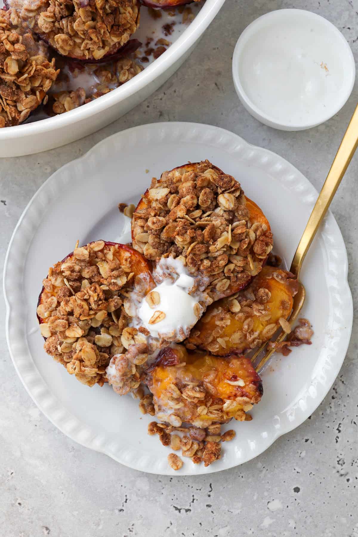 Air fryer peaches on plate with ice cream and fork cutting into one.