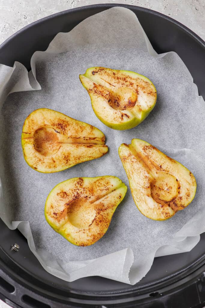 Pears rubbed with cinnamon in air fryer basket.