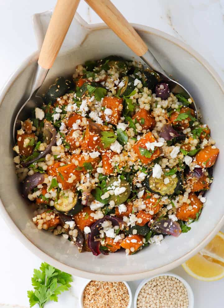 Pumpkin couscous salad in a mixing bowl with spoons.