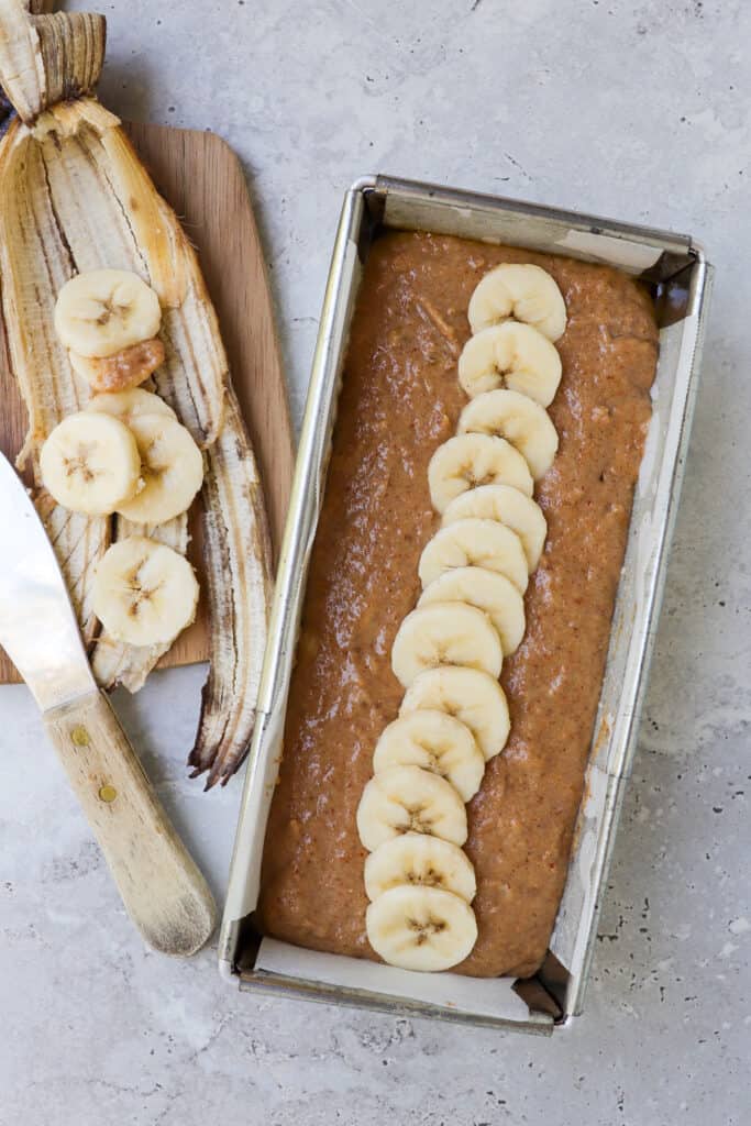 Bananas bread mixture in pan topped with banana sliced.