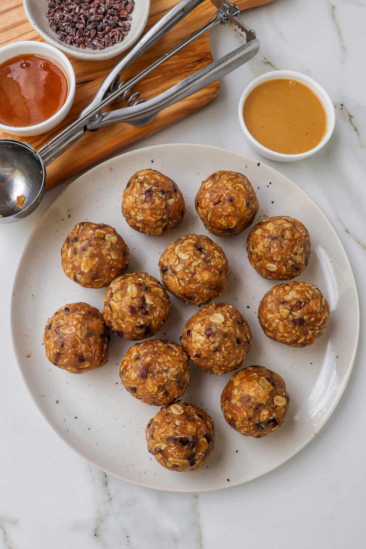 Bliss balls on a plate with peanut butter and ingredients on the side.