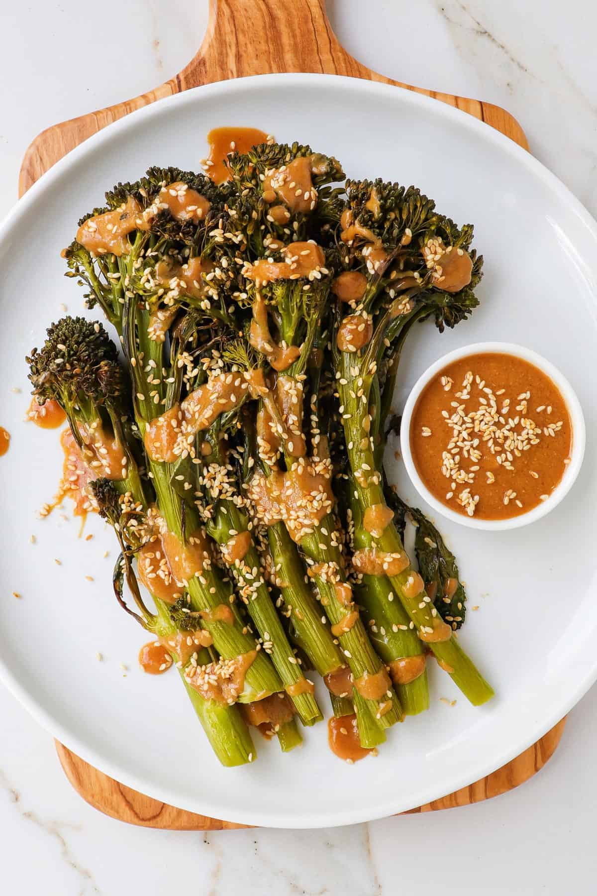 Tenderstem broccoli on a wooden board and plate with miso sauce drizzled on top