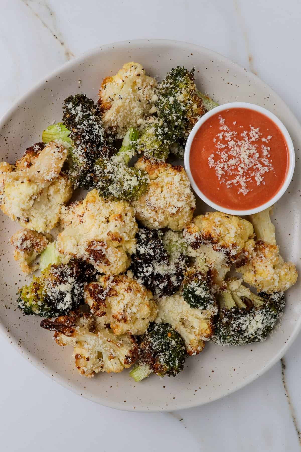 Air fried cauliflower and broccoli on a plate with red sauce.