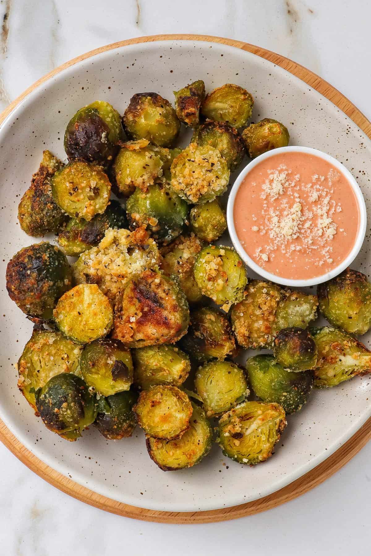 Air fryer roasted Brussels sprouts on a wooden board with creamy tomato sauce.