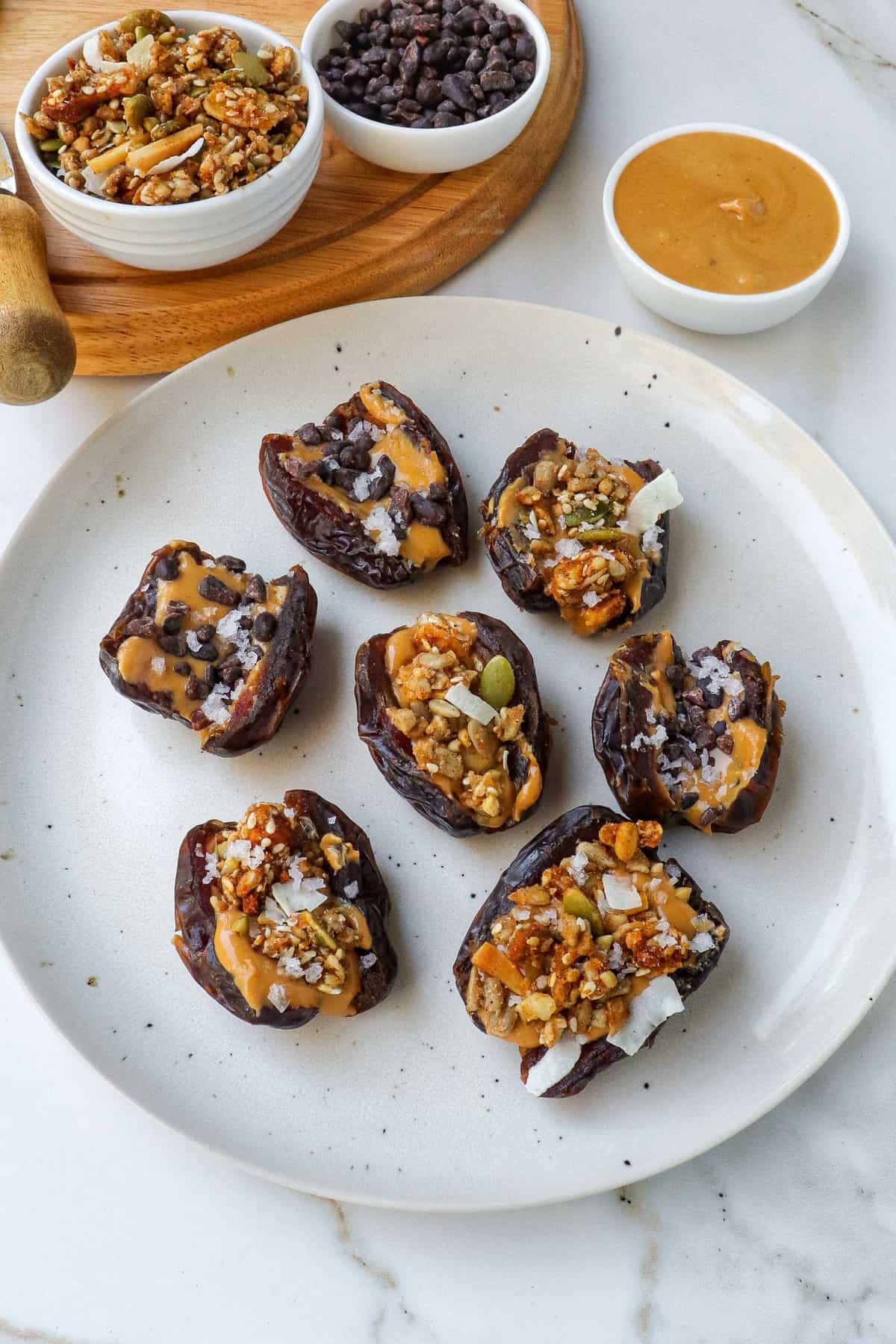 Side shot of peanut butter stuffed dates with granola and cacao nibs on a plate.
