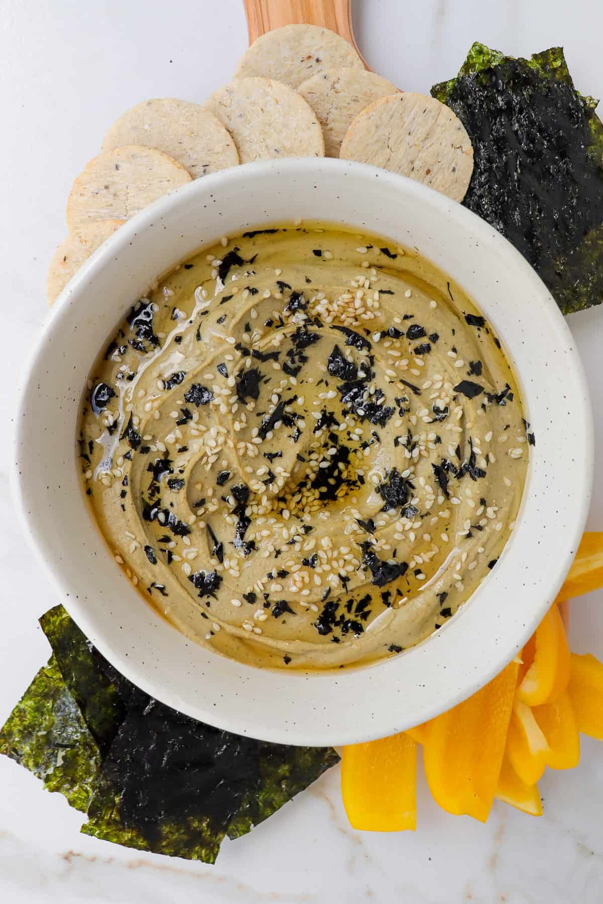 Hummus in a bowl with seaweed, crackers and peppers on the sides.