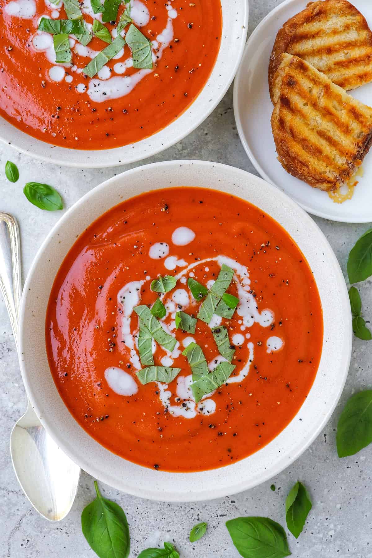 Two bowls of tomato soup with shredded basil leaves and coconut cream drizzled on top.