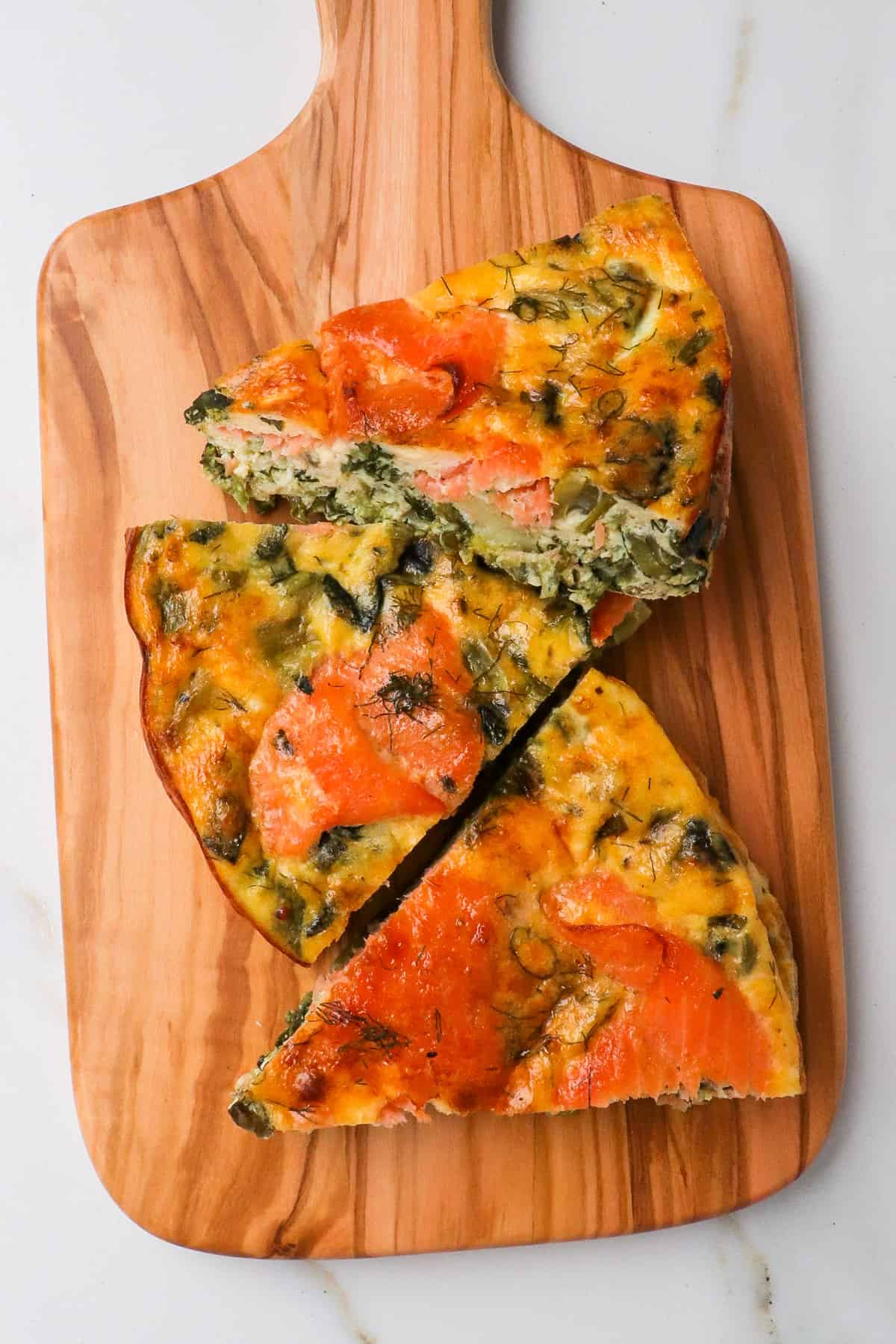 Slices of salmon spinach quiche on a wooden board.