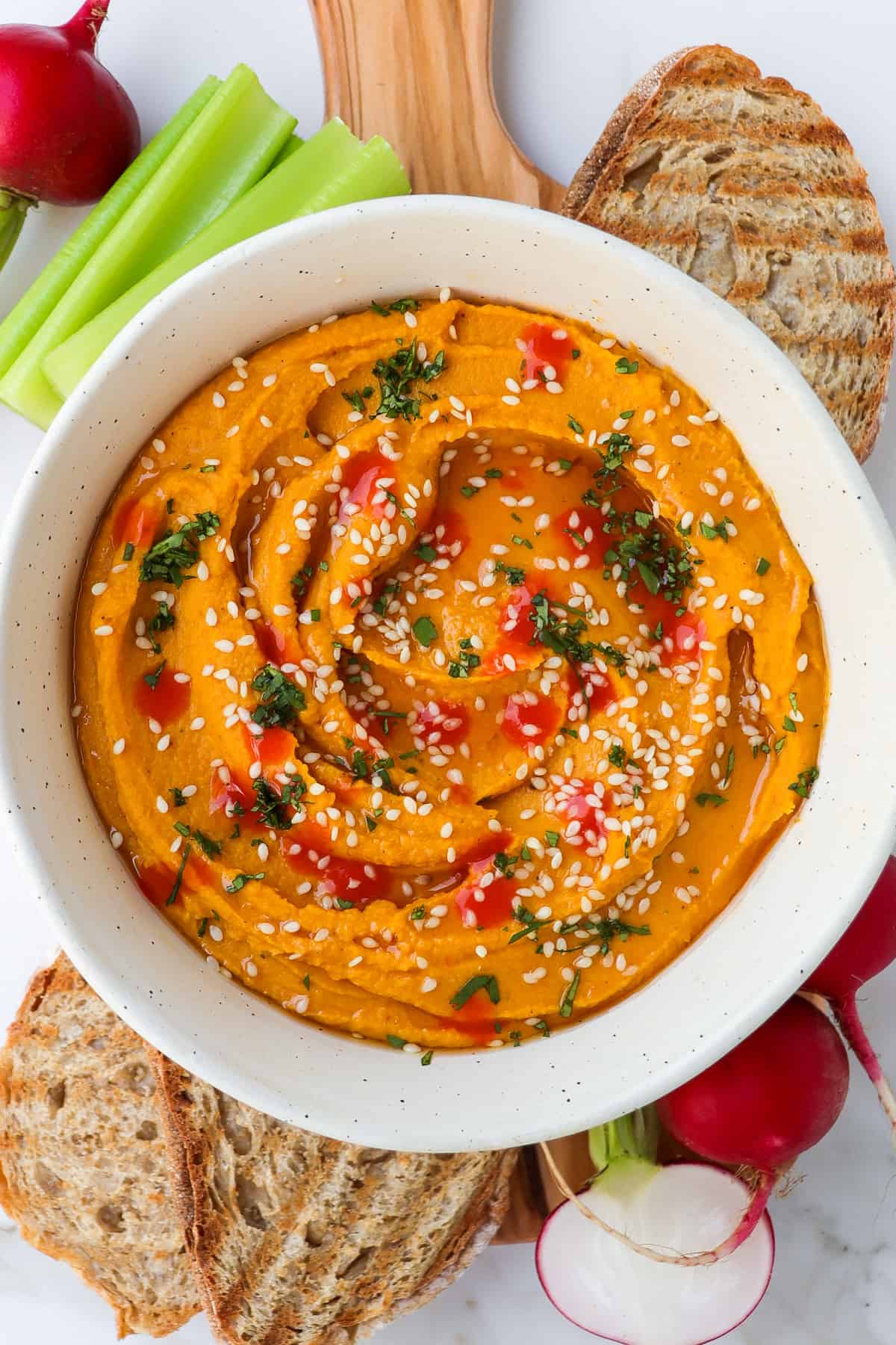 Carrot hummus in a bowl with vegetable crudités and toasted bread.