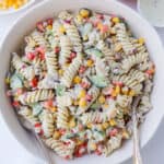 Creamy pasta in a bowl with capsicum, corn kernels, herbs and dressing on the side.