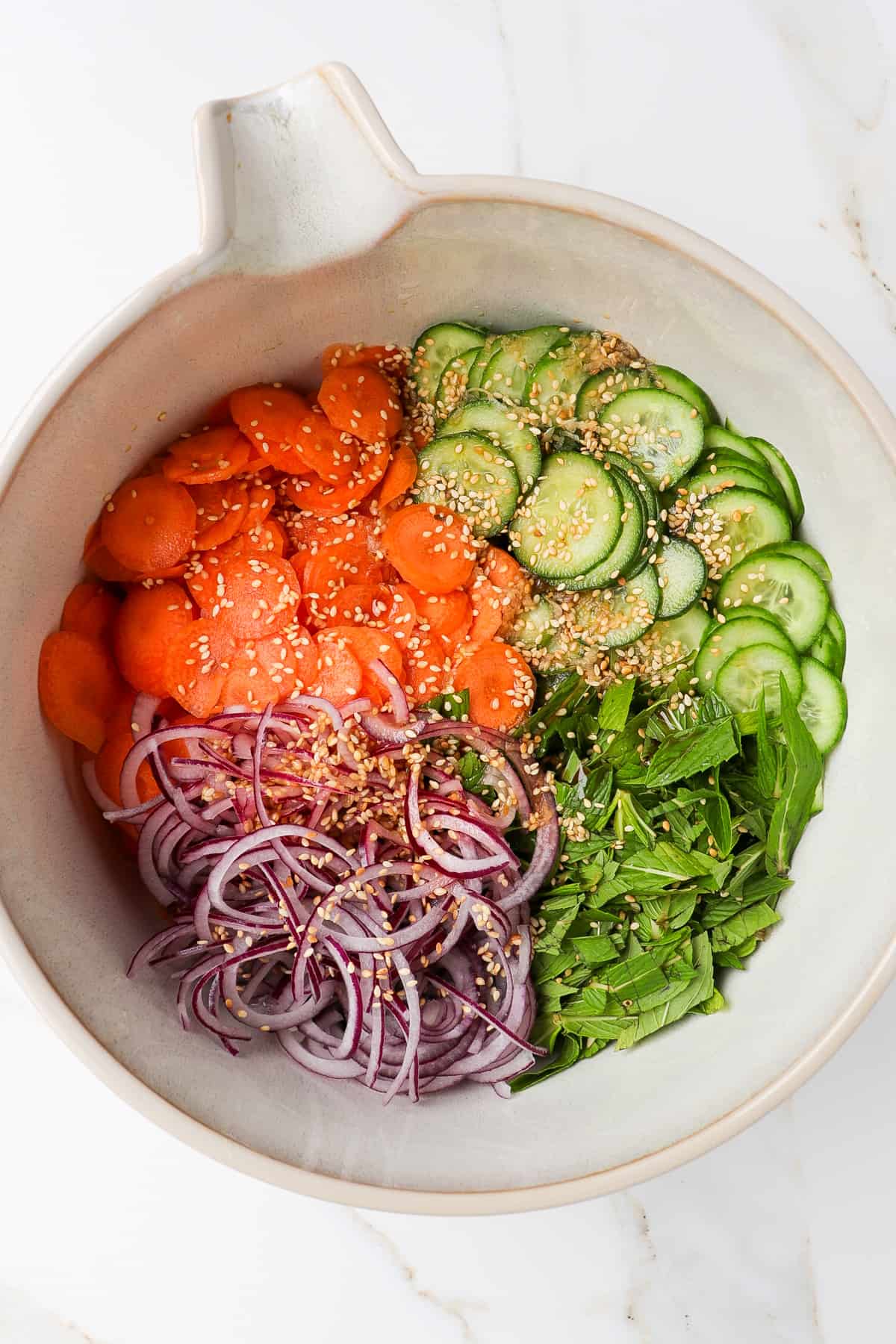 Cucumbers, carrots, red onions, mint and toasted sesame seeds in a bowl.
