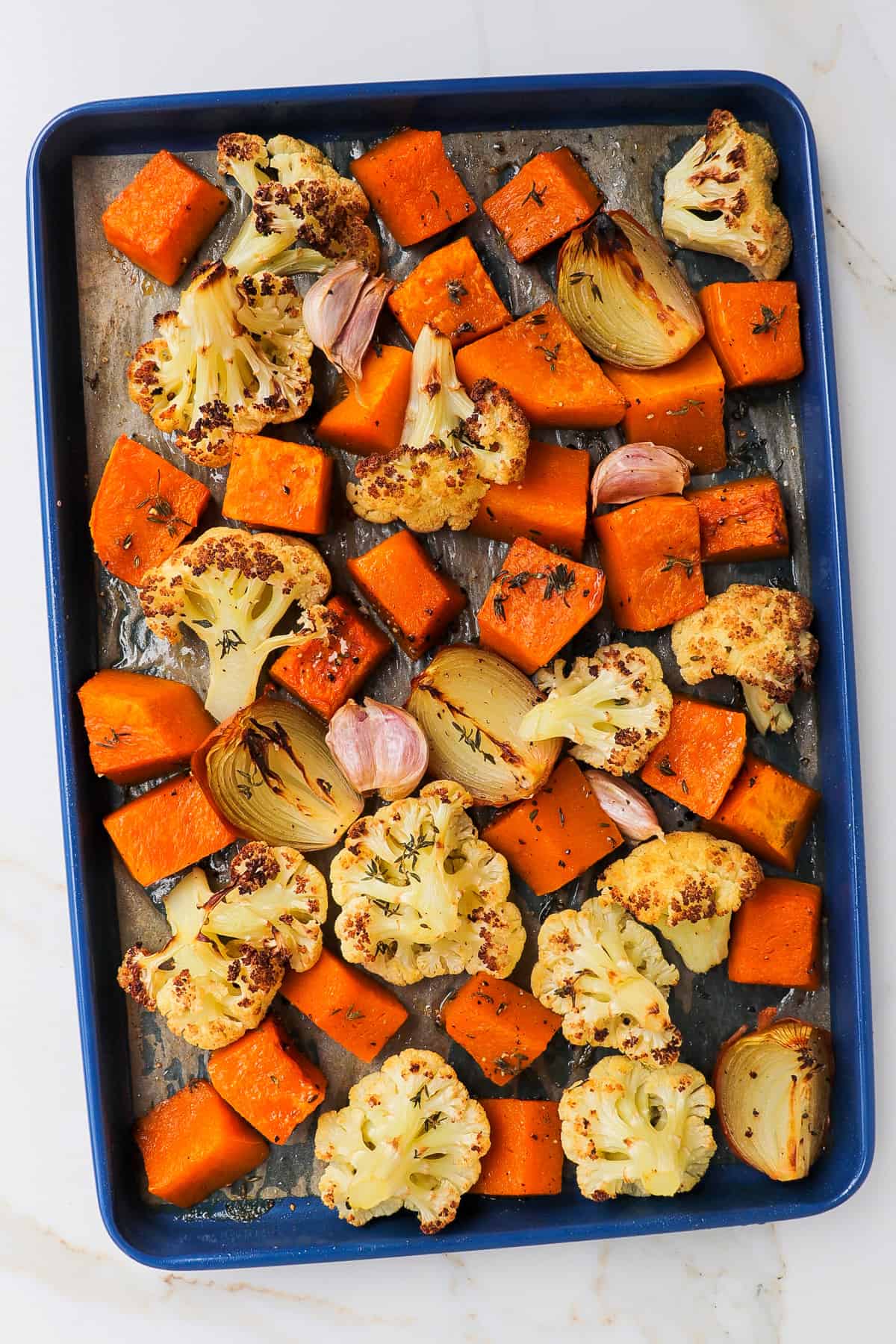 Roasted cauliflower florets, cubed pumpkin, onions and garlic on a baking tray.