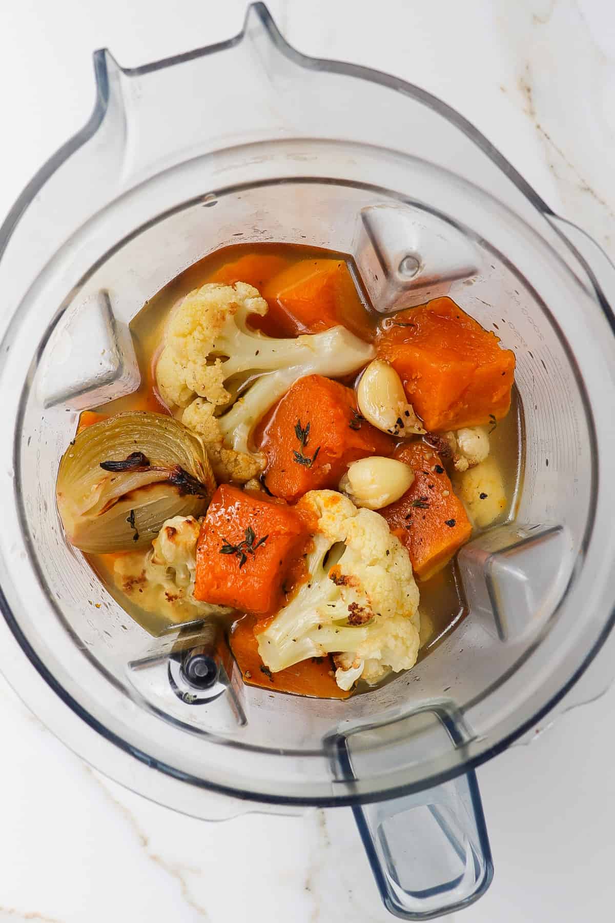 Roasted vegetables in a blender jug with thyme leaves and vegetable stock.