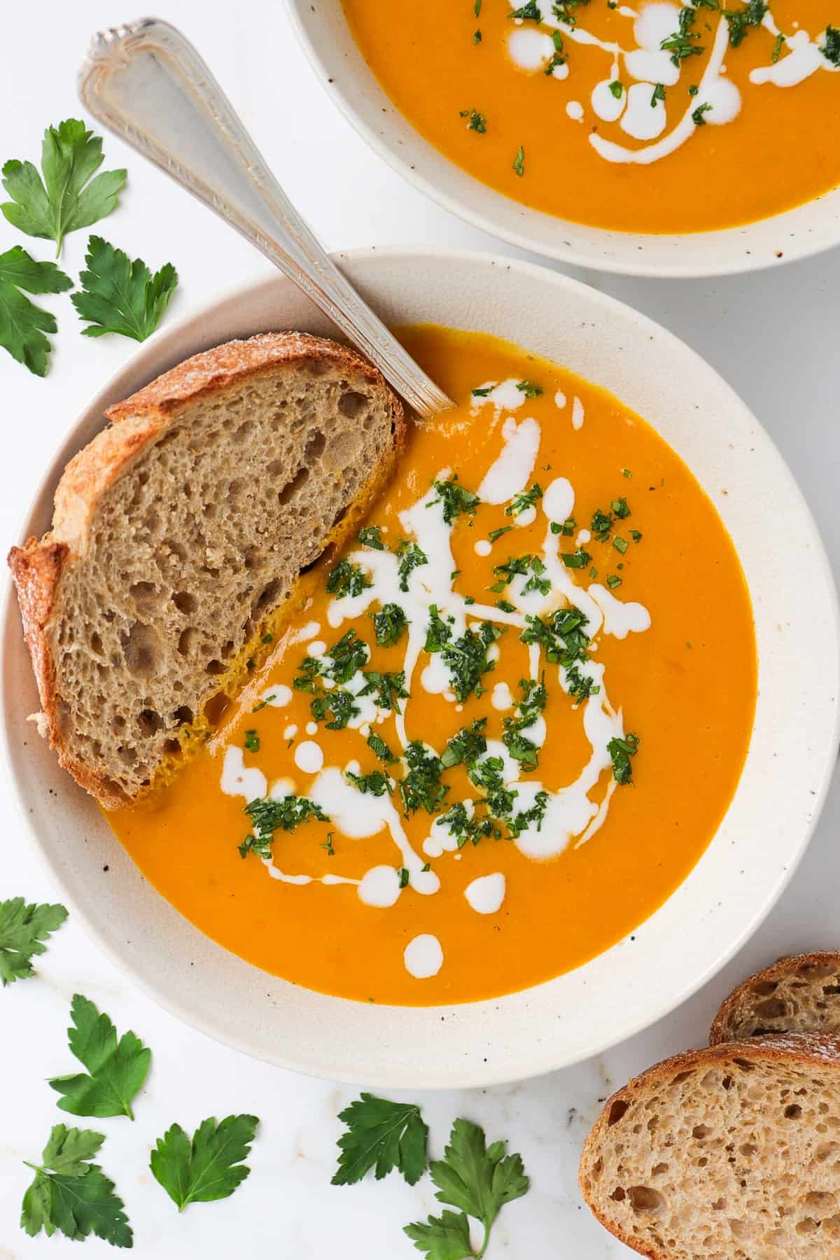 Carrot pumpkin soup in a bowl with sourdough bread slice on top with a spoon.