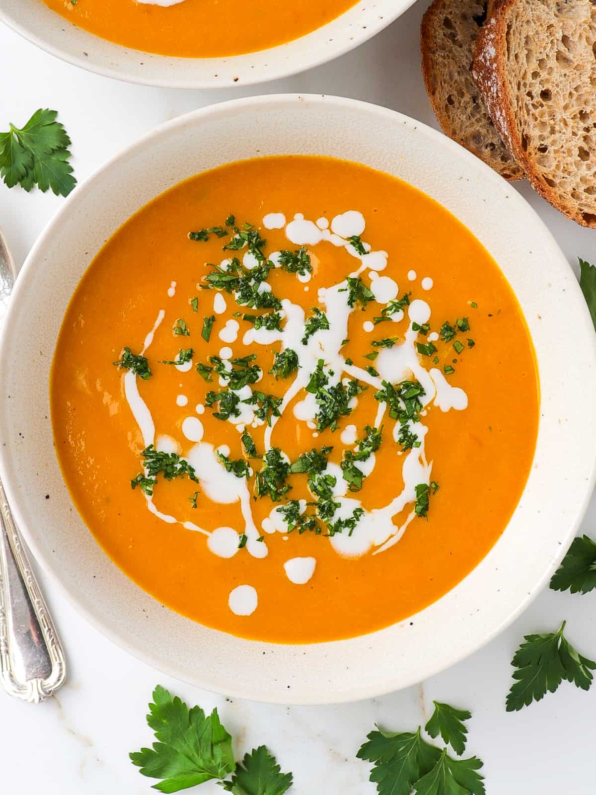 Carrot pumpkin soup in bowls with cream and parsley on top.
