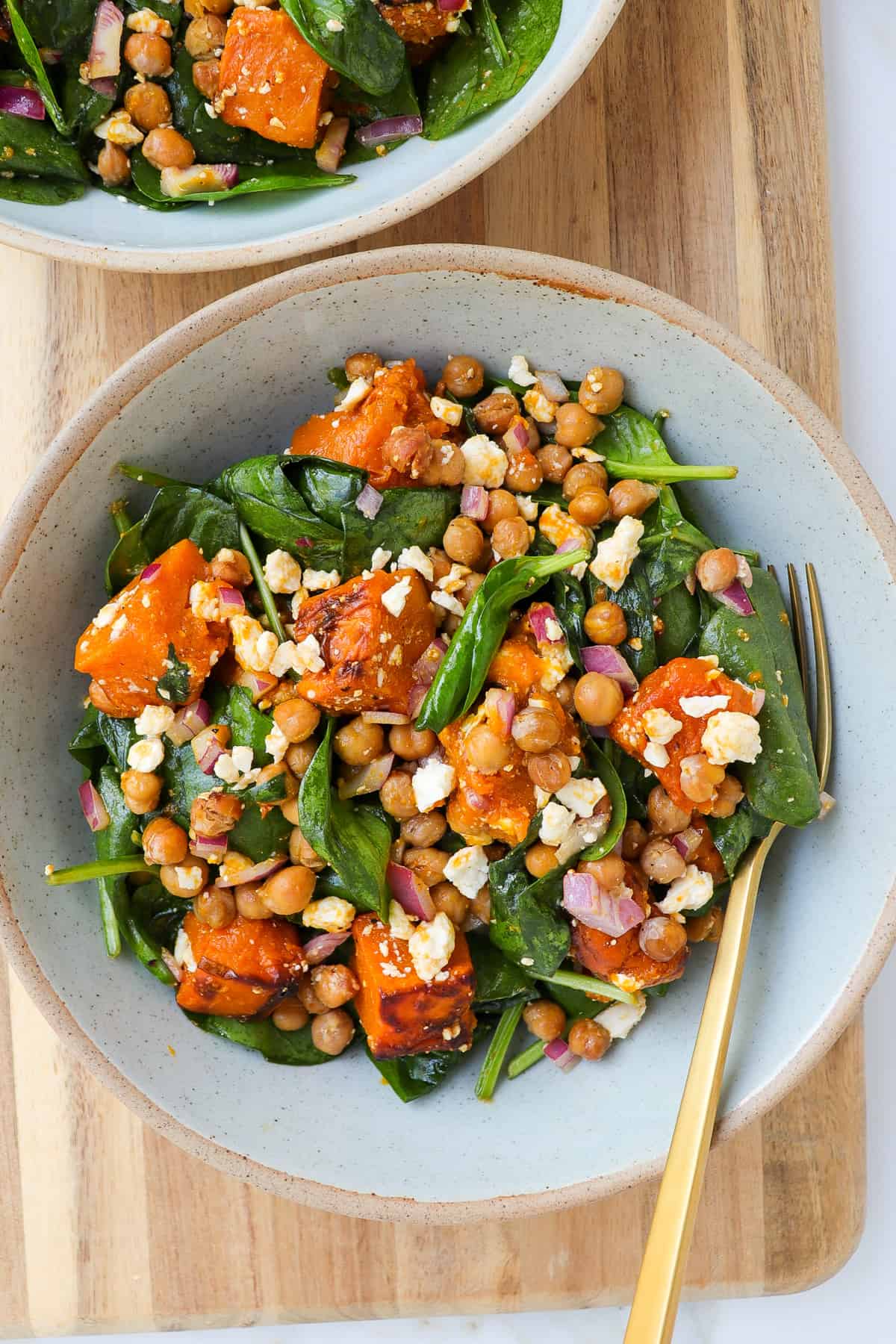 Chickpea pumpkin salad in a bowl on a wooden board with a gold fork.