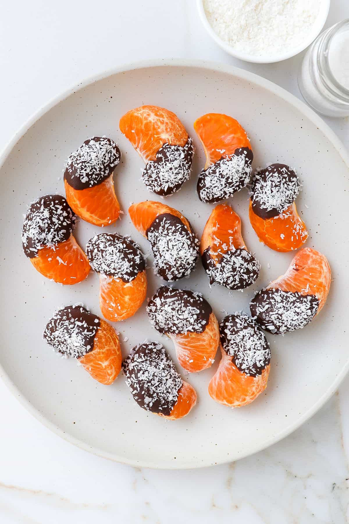 Chocolate covered orange pieces sprinkled with coconut on a plate.