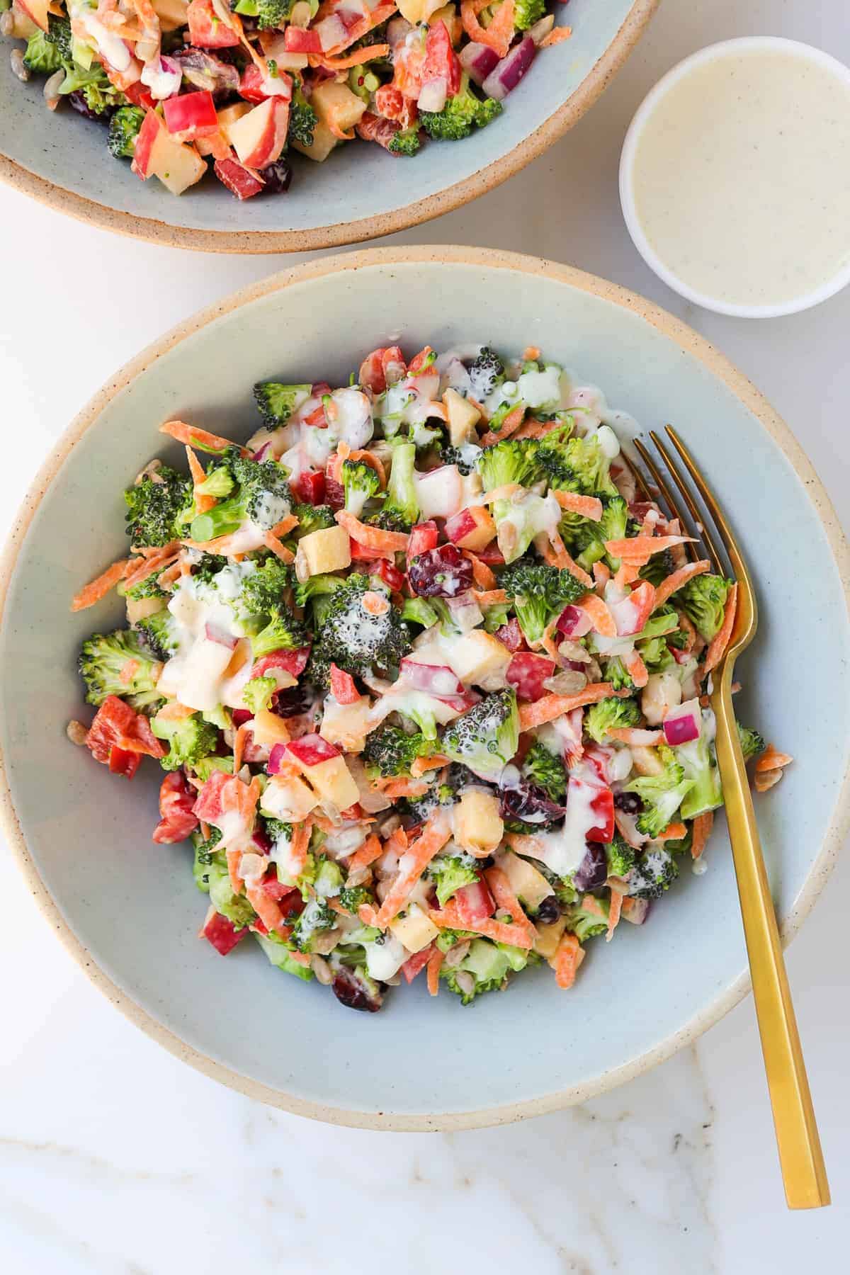 Broccoli salad in a bowl with a fork and extra tahini dressing in a little dish.