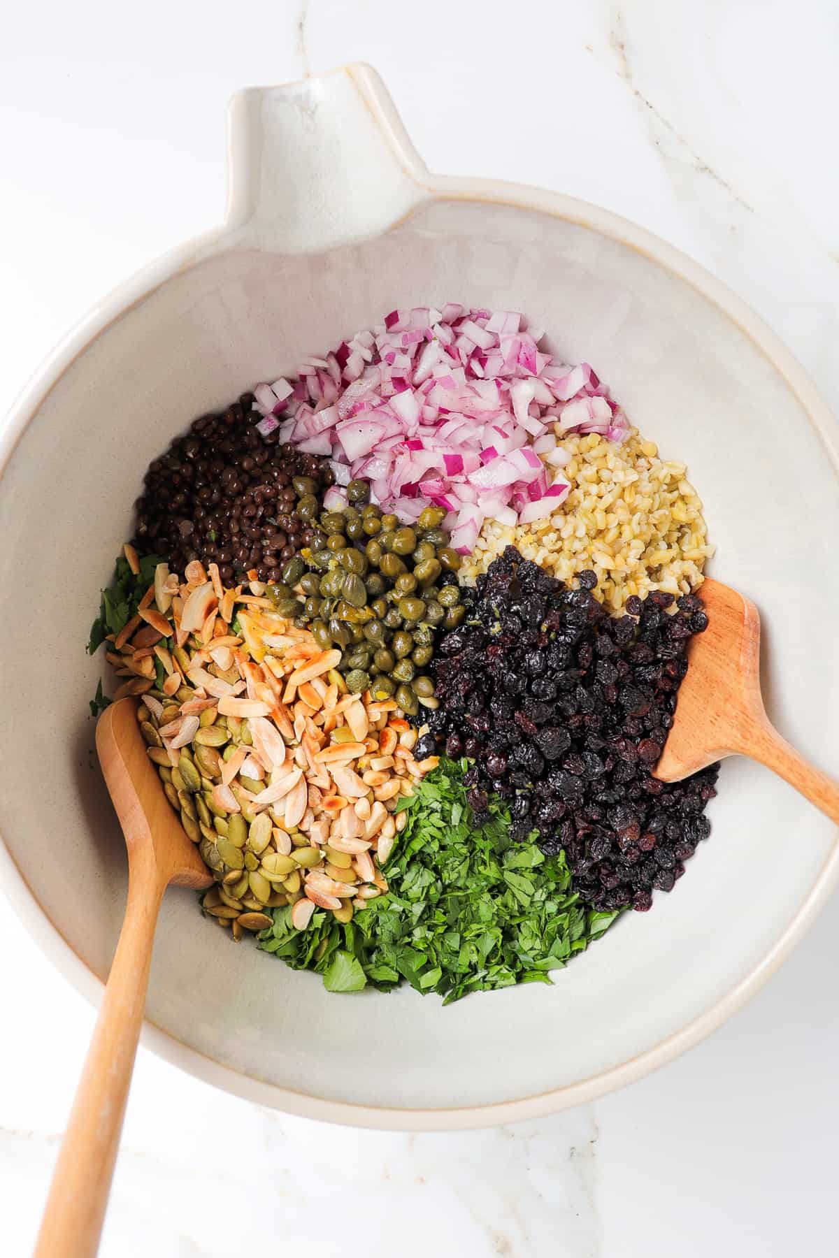 Grain salad ingredients in a mixing bowl with wooden spoons.