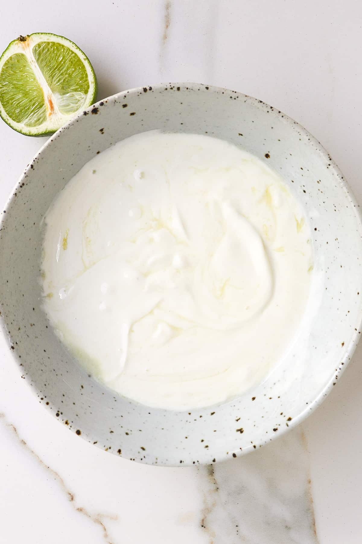 Yoghurt sauce in a bowl with a half a lime on the side.