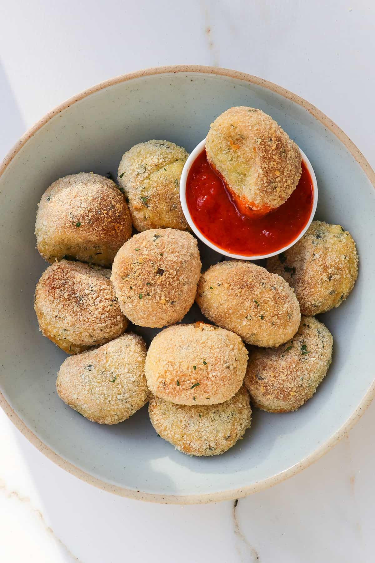 Potato croquettes in a bowl with one dipped in marinara sauce.