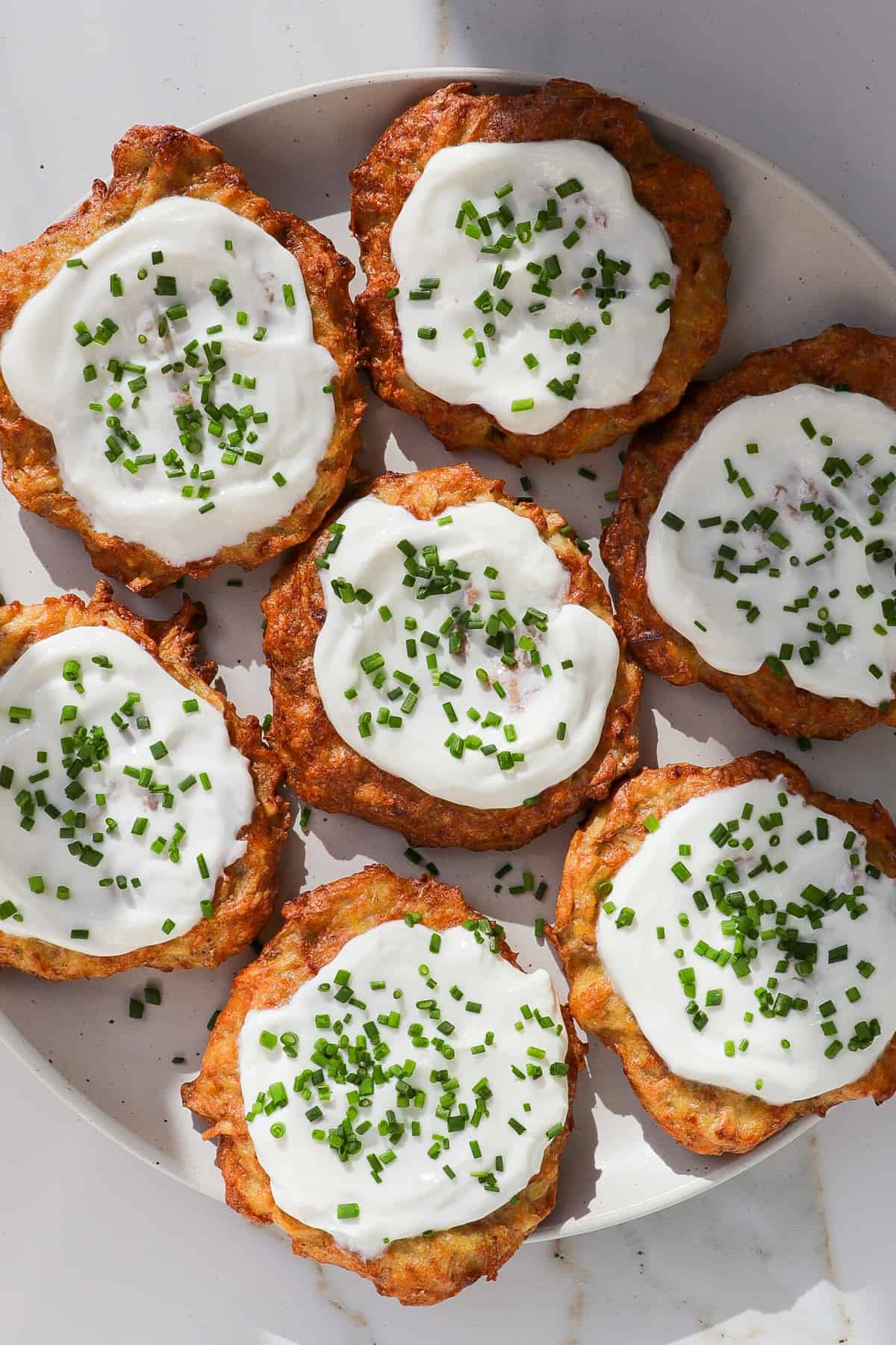 Potato fritters on a plate topped with greek yoghurt and chives.