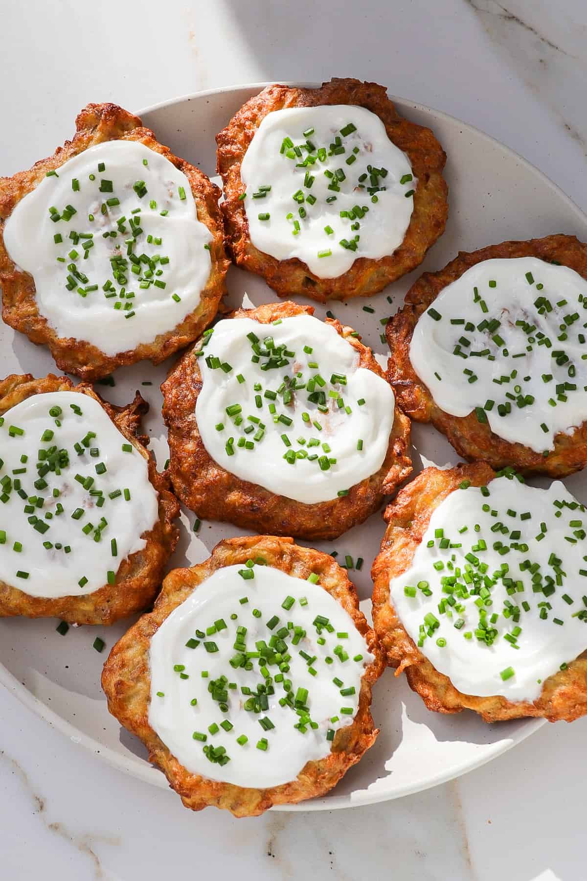 Air fryer potato fritters on a plate topped with greek yoghurt and chives.