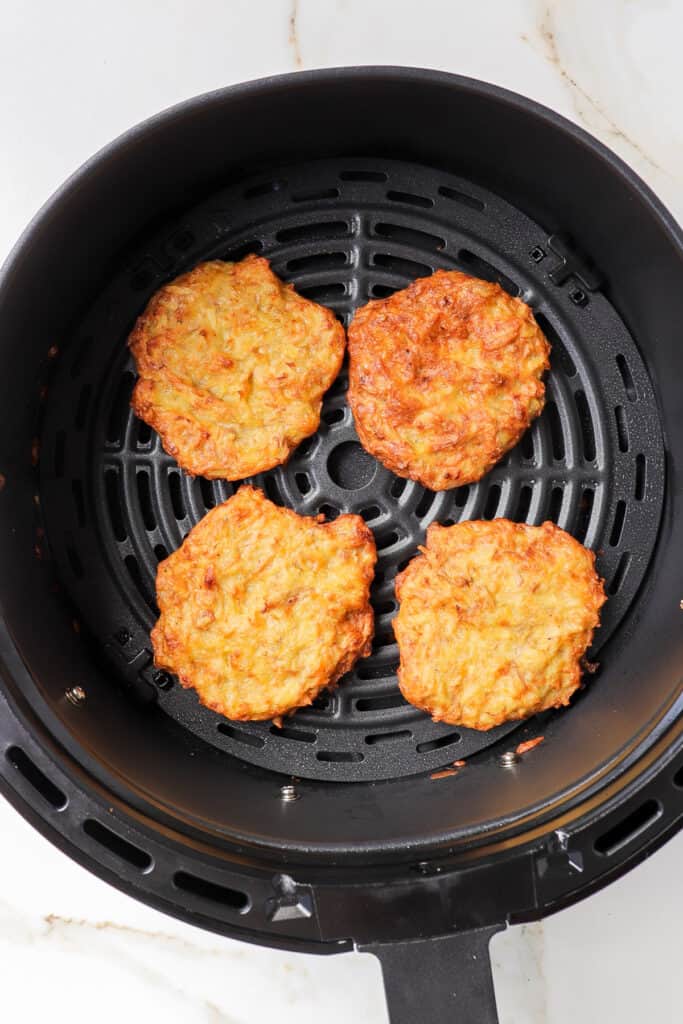 Cooked potato fritters in air fryer basket.