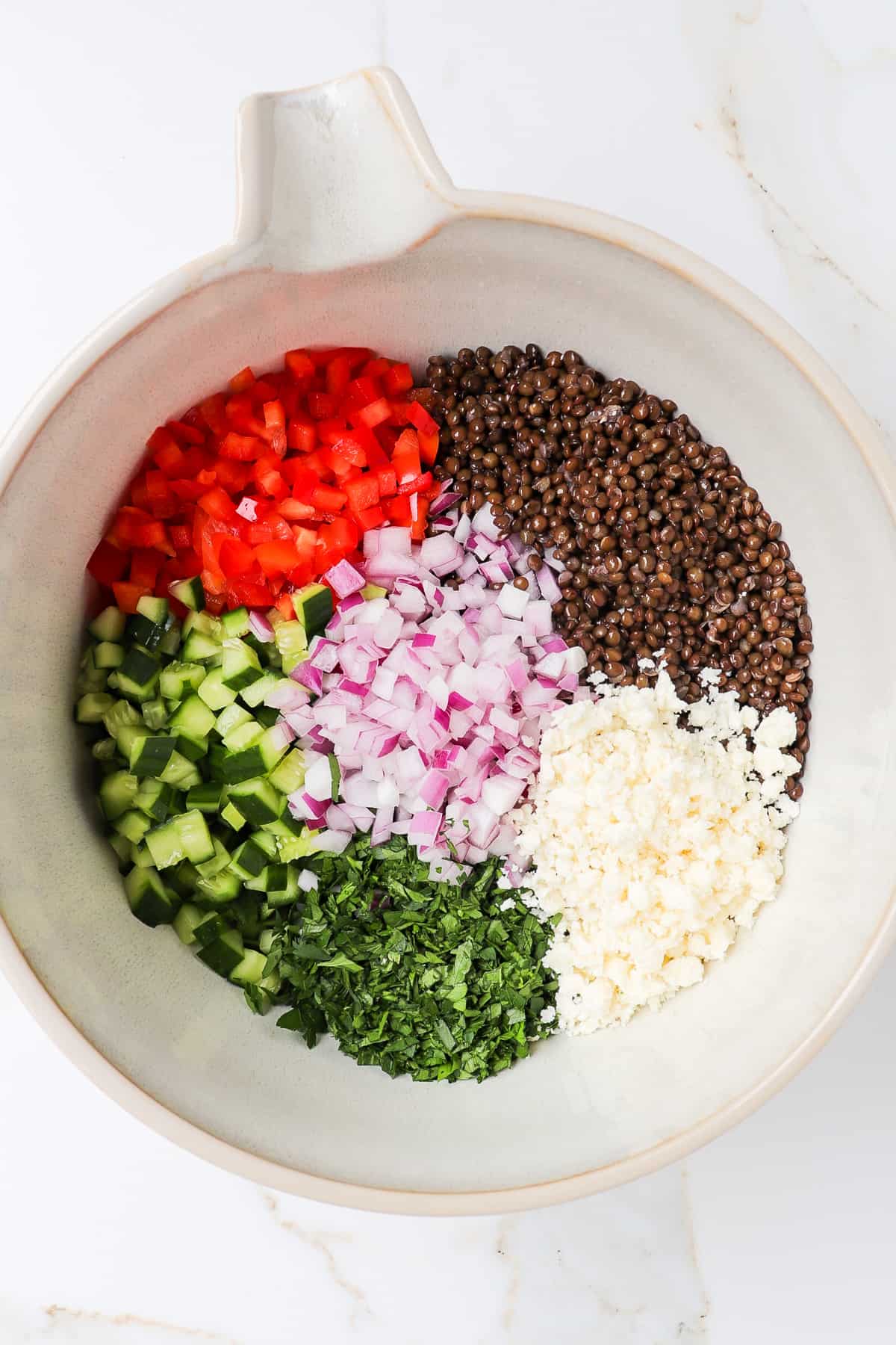 Black lentils, red capsicum, cucumber, parsley, red onion and crumbed feta cheese in a large mixing bowl.