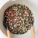Black lentil salad in a mixing bowl with wooden spoons.