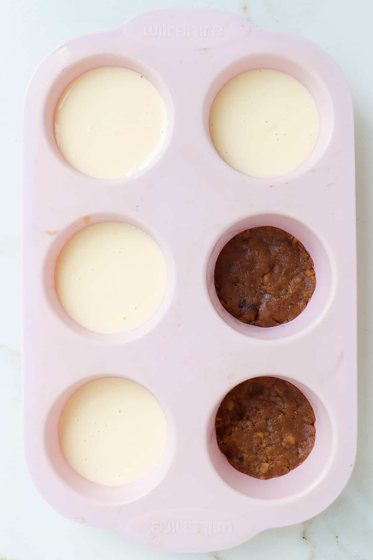 Cookie base pressed in silicon muffin pan cavities with four filled with cheesecake filling