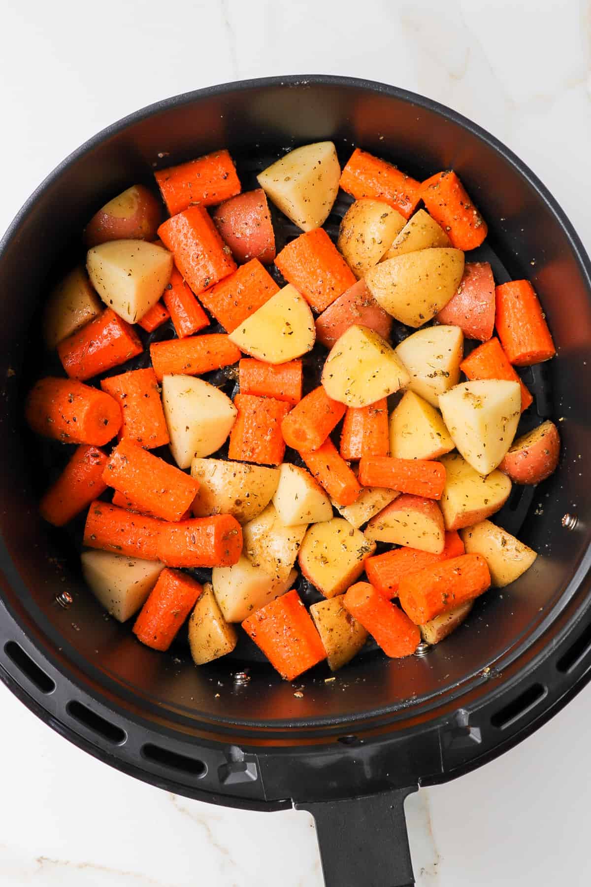 Uncooked carrots and potatoes in air fryer basket.