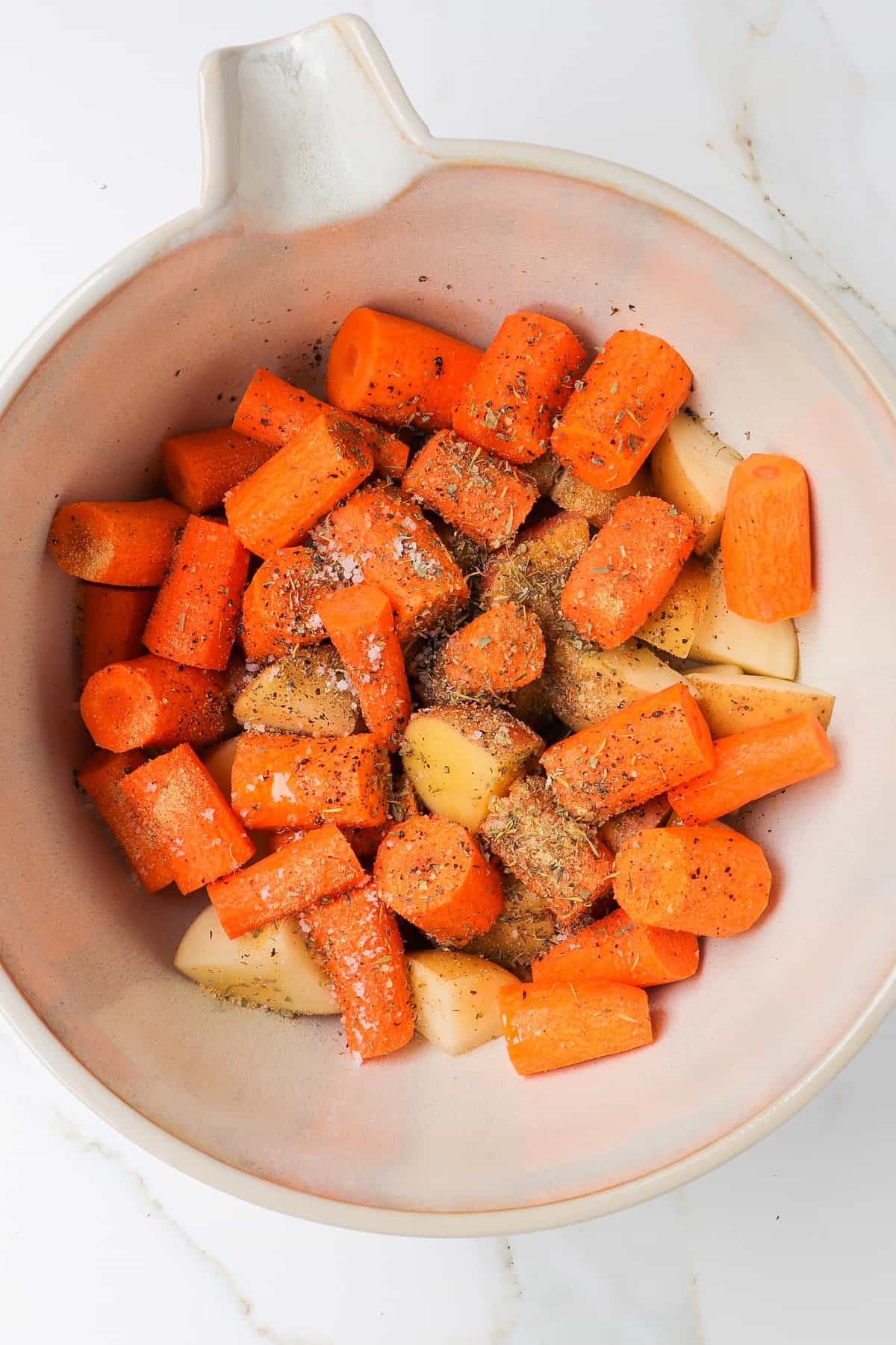 Carrots and potatoes in a bowl with seasonings.
