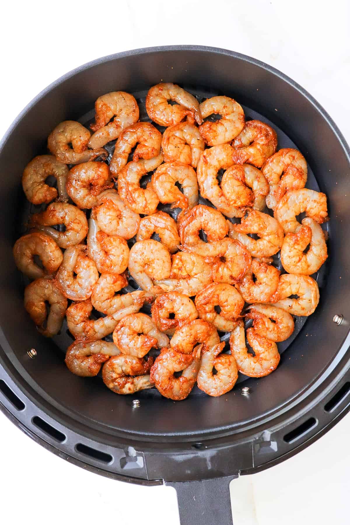 Seasoned shrimp in air fryer basket.