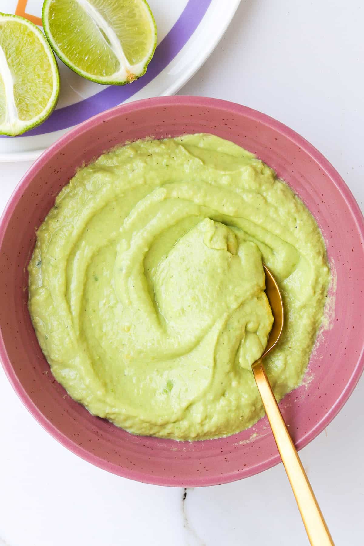 Avocado crema in a pink bowl with a gold spoon.