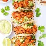 Shrimp tacos with with slaw and avocado crema in a dish on the side.