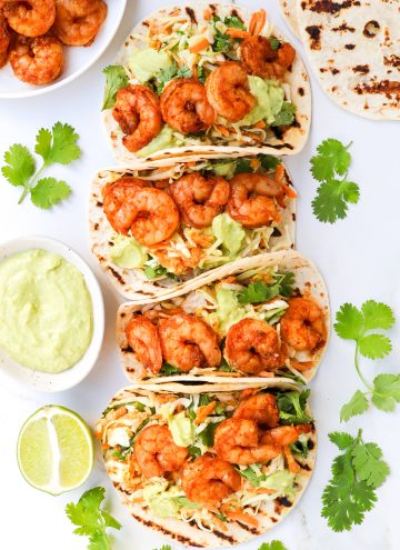 Shrimp tacos with with slaw and avocado crema in a dish on the side.