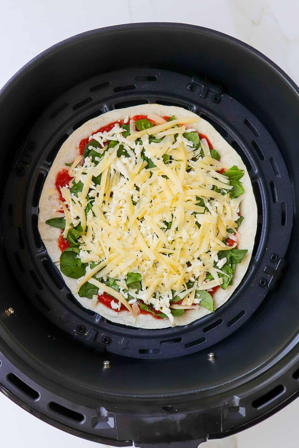 Tortilla pizza in air fryer basket.