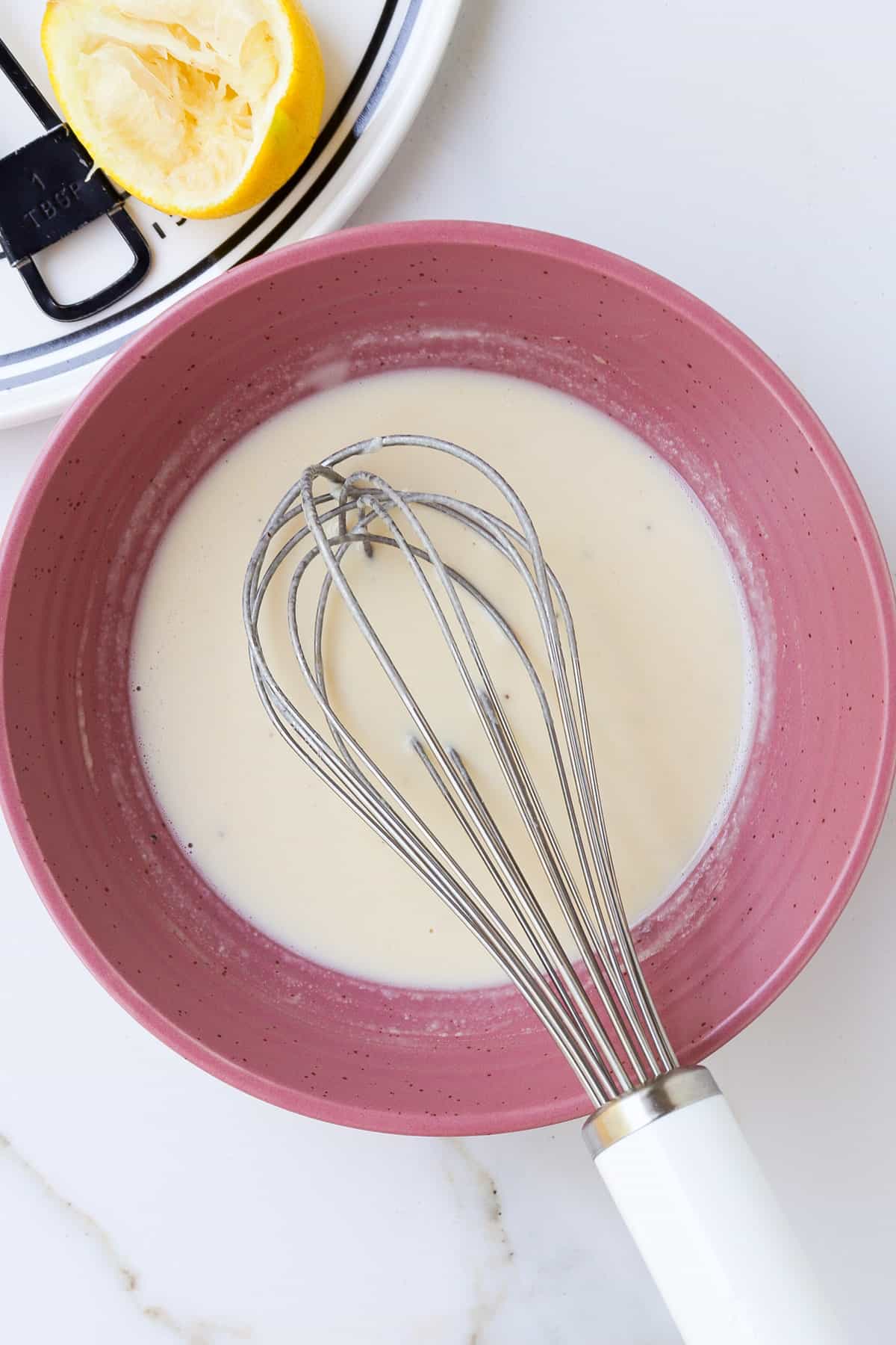 Lemon tahini dressing in a pink bowl with a whisk.
